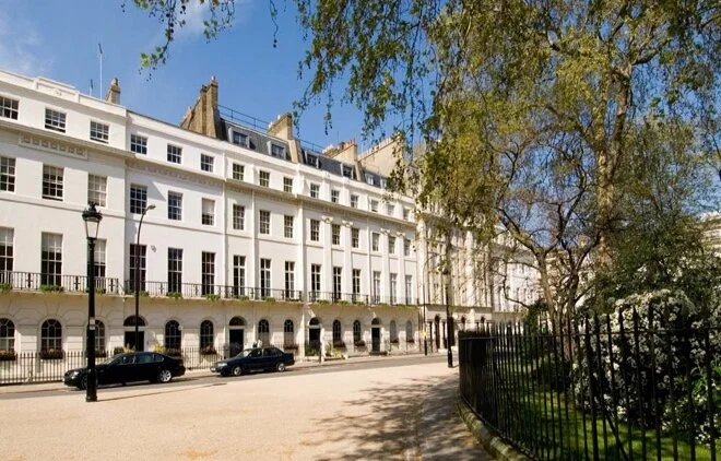 Grand white Georgian stucco townhouses lining Fitzroy Square, London, with mature spring trees and iron railings.