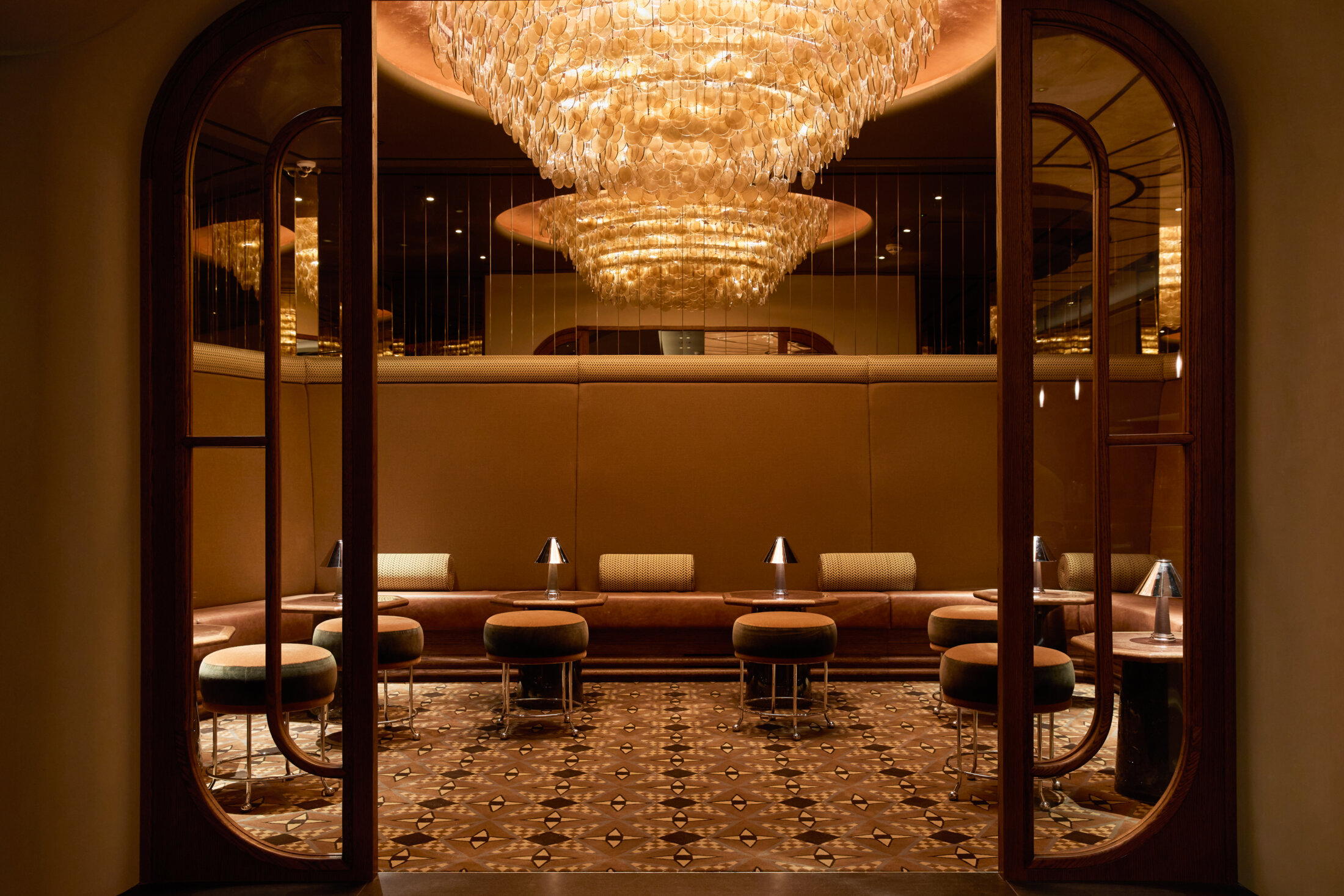 Opulent amber-lit cocktail bar with tiered glass chandelier and leather banquettes at The Newman private event spaces Fitzrovia